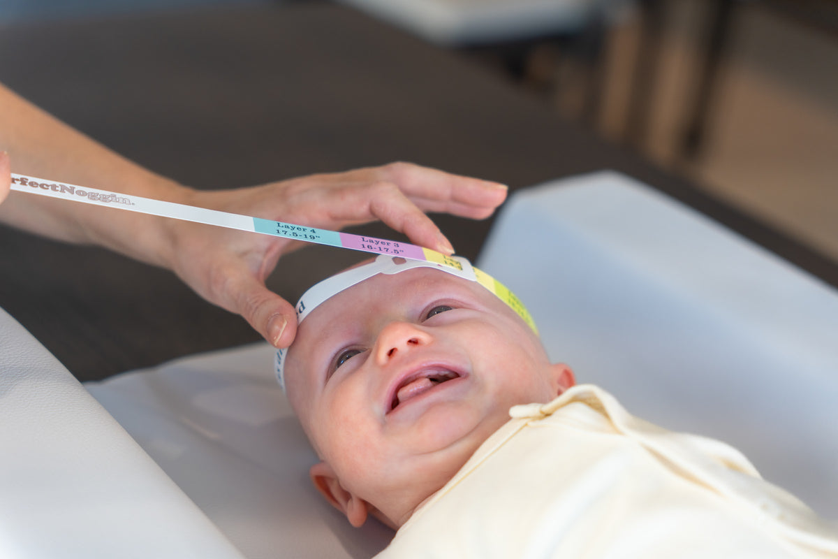 A parent threading a tape measure around a laughing baby's head on a change mat