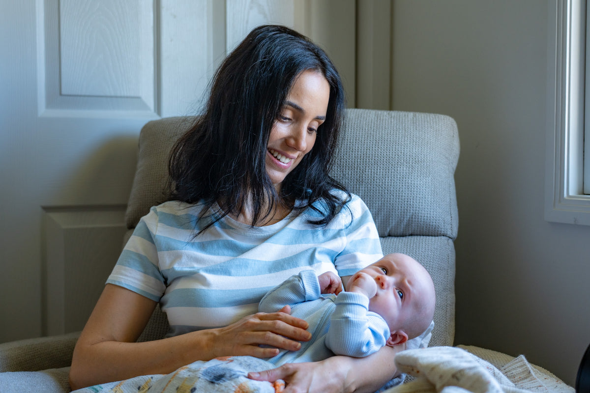 A mum in an armchair holding her newborn baby and smiling