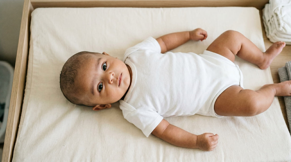 A baby lying on their back on a mattress, seen from above