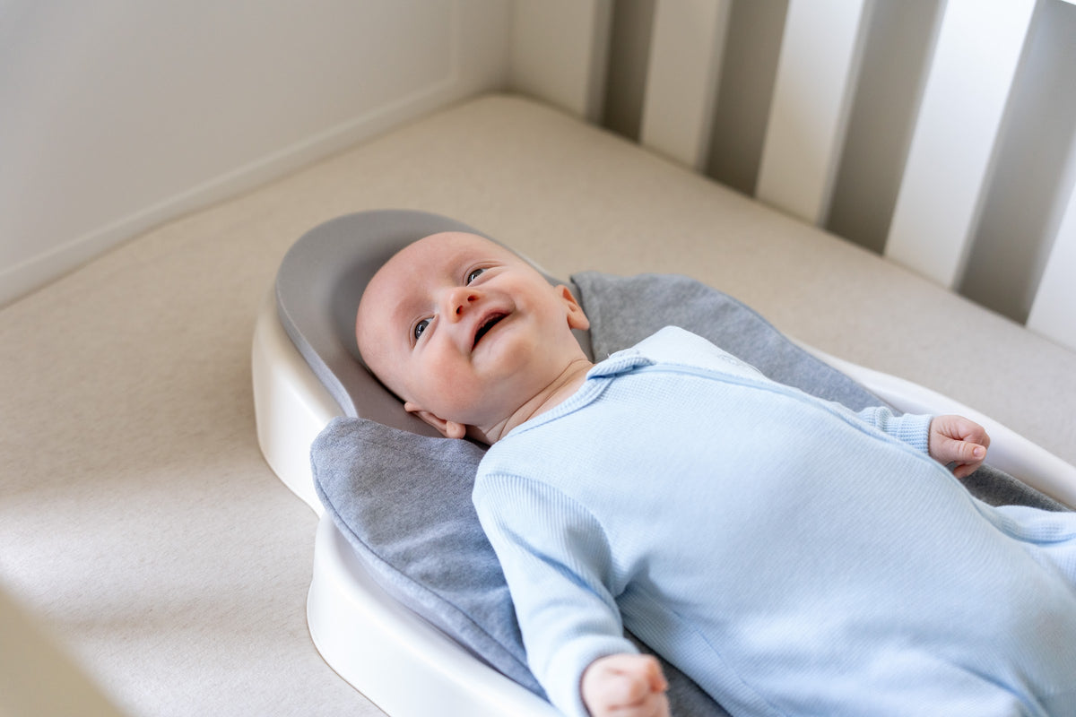 A baby lying on his back on the Perfect Noggin in a cot