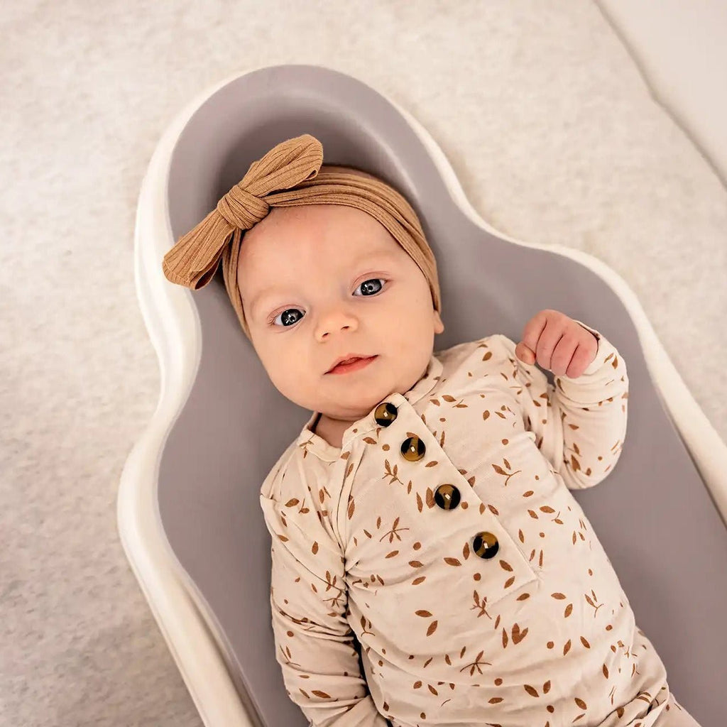 Smiling baby with a hair bow lying on their back on the Perfect Noggin contoured head shaping surface