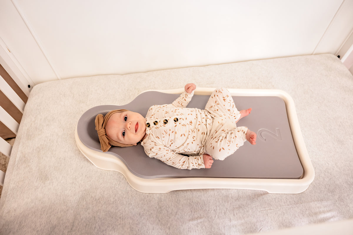 A baby lying on their back on the Perfect Noggin in a cot