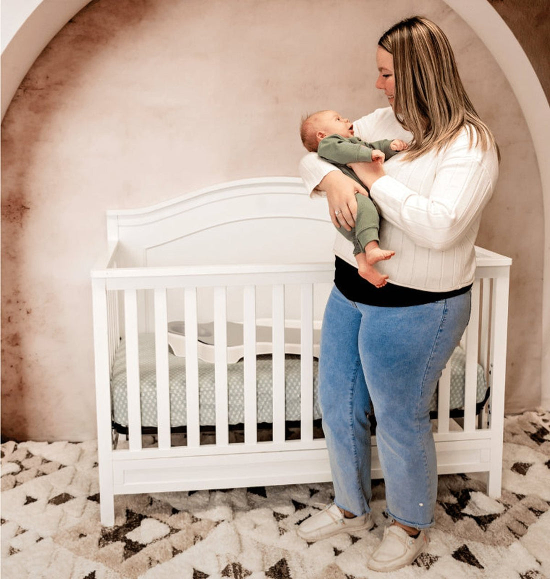 A mum holding her baby beside a cot